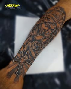 a man's arm with a cross and roses tattoo design on the left forearm