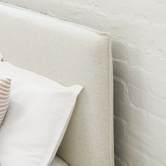 a white bed with two pillows on top of it next to a brick wall and window