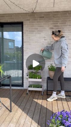 a woman is watering plants on the porch