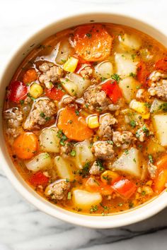 a white bowl filled with meat and vegetable soup on top of a marble countertop