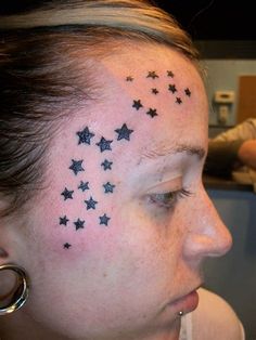 a woman with black stars on her face and behind her ear, looking to the side