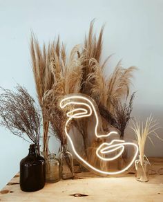 a wooden table topped with vases filled with dry grass and lights in the shape of a face