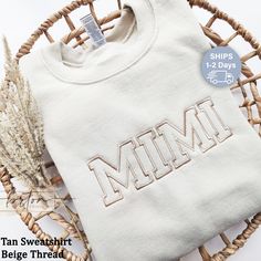 a white t - shirt with the word mimi on it sitting next to some dried plants