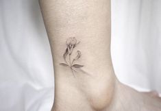 a small flower tattoo on the ankle is shown in black and grey ink, with one single flower at the top