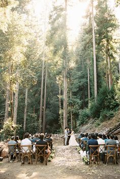 an outdoor ceremony in the woods with people sitting on chairs and looking at each other