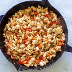 a skillet filled with chicken and vegetables on top of a white countertop next to a wooden spoon