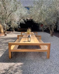 a wooden table sitting in the middle of a gravel covered area next to some trees