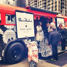 people are standing in line to get on a tour bus that is painted red and white