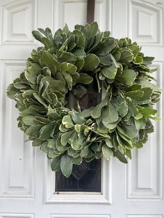 a wreath hanging on the front door of a house with white doors and green leaves