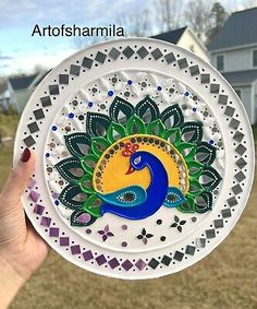 a person holding up a plate with a peacock on it in front of a house