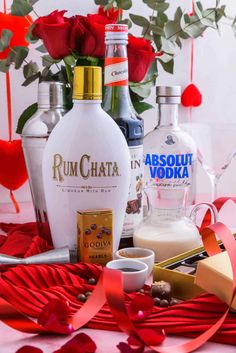 bottles of vodka, chocolates and roses on a table with red ribbon around it