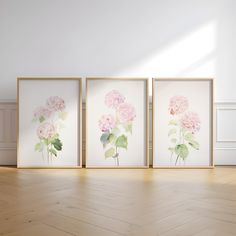 three pink flowers are displayed in four frames on the floor next to an empty wall