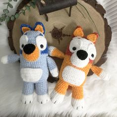 two crocheted stuffed animals sitting next to each other in front of a tree stump