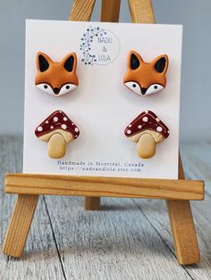 a pair of fox and mushroom studs on a wooden easel with a card