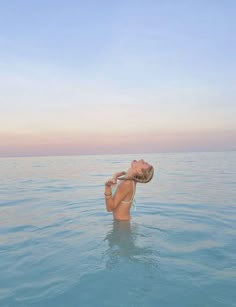 a woman floating in the ocean with her head above water and drinking from a bottle