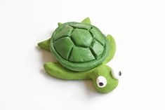 a green stuffed turtle laying on top of a white surface