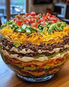 a layered salad in a glass bowl on top of a wooden table