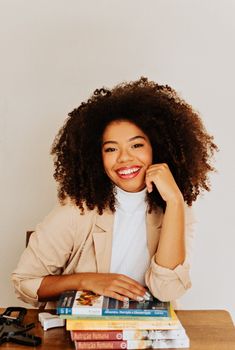 a woman sitting at a table with books on her lap and smiling for the camera