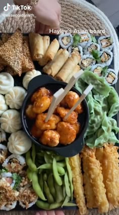 there is a platter with many different foods on the table and someone holding chopsticks in their hand