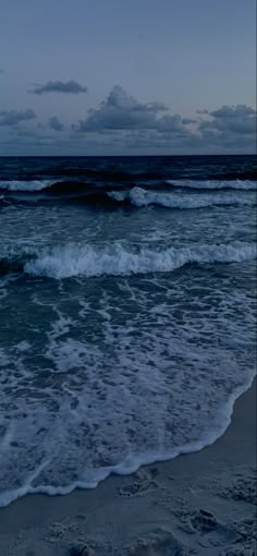 the ocean with waves coming in to shore at night time, under a cloudy sky