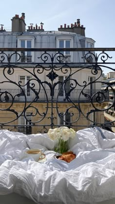 a bed with white sheets and flowers on it in front of an iron balcony railing