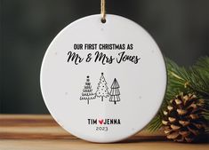 a white ornament hanging from a pine tree with the words our first christmas as mr and mrs jones