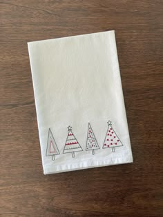 three small christmas trees on a white napkin sitting on top of a wooden table next to a cup