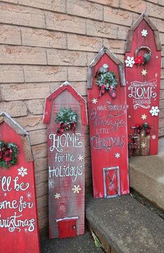 three red wooden signs with christmas decorations on them sitting next to a brick wall in front of a house