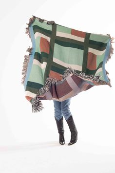 a woman is holding a multicolored blanket over her head while standing in front of a white background