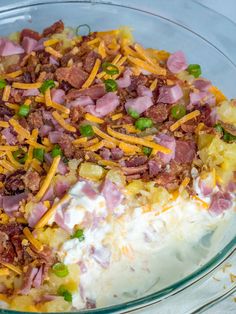 a glass bowl filled with mashed potatoes covered in cheese and meats, topped with green onions