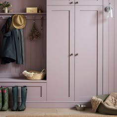 a coat rack with several coats hanging on it next to some boots and hats in front of a pink wall