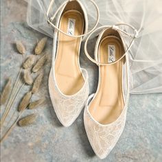 a pair of white lace shoes sitting on top of a table next to dried flowers