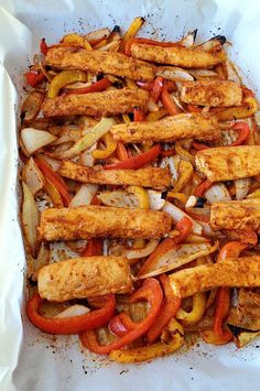 chicken fajitas with peppers and onions in a white pan on top of parchment paper