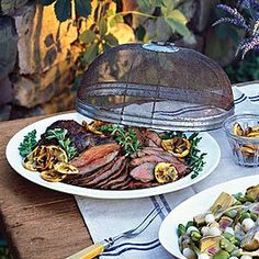 a table topped with plates of food next to a bbq covered in meat and vegetables