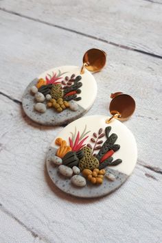 two white earrings with colorful flowers and rocks on the bottom, sitting on a wooden surface