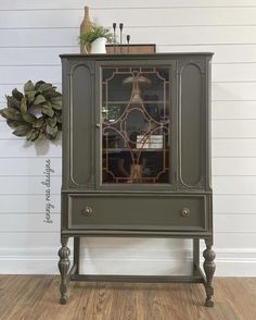 a green cabinet with an ornate glass door on the top and bottom, in front of a white wall