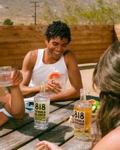 a man sitting at a picnic table with two bottles of alcohol