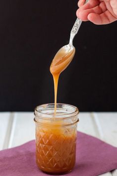 someone is pouring caramel sauce into a mason jar on a purple napkin with a spoon