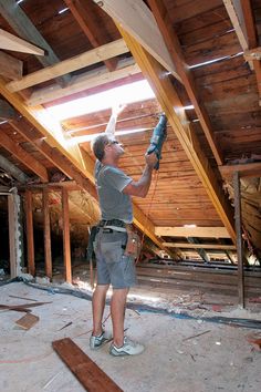 a man in grey shirt and gray shorts working on wood beams inside an unfinished building