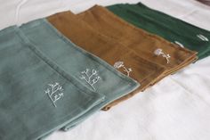 four different colored napkins with embroidered designs on them sitting on a white bed sheet