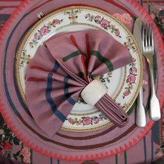 a table setting with pink napkins, silverware and flowers on the placemat