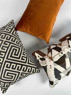 three decorative pillows sitting on top of a white bed next to each other and one brown pillow