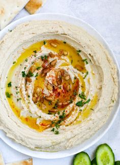 hummus in a white bowl surrounded by sliced cucumber and pita chips