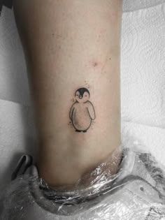 a small penguin tattoo on the ankle is shown in black and grey ink, with a tiny dot at the bottom