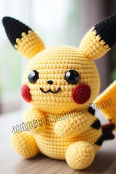 a crocheted pikachu sitting on top of a wooden table next to a window