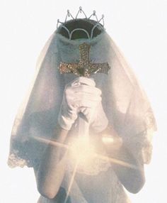 a woman wearing a veil and holding a cross in her hands with the sun shining behind her