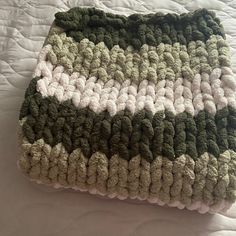 a green and white crocheted blanket sitting on top of a bed next to a pillow