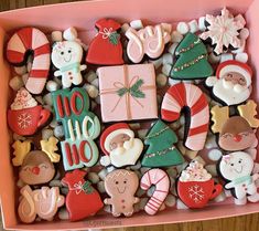 a pink box filled with lots of different decorated christmas cookies on top of a wooden table