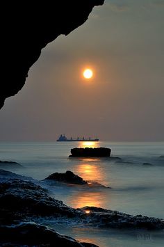 the sun is setting over an ocean with rocks