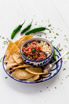 a bowl of salsa with tortilla chips and green chili peppers on the side